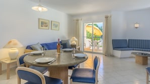 Ein Essbereich mit rundem Tisch, Stühlen und einer Couch. Ein Fenster mit Vorhängen bietet einen Blick ins Freie.