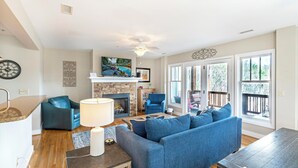 Una sala de estar con chimenea, sofá azul y televisor sobre una repisa.