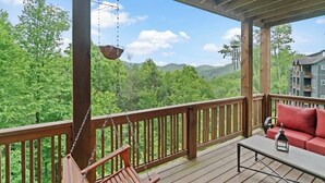 Una terraza de madera con una silla colgante y un sofá, con vistas a un paisaje boscoso.