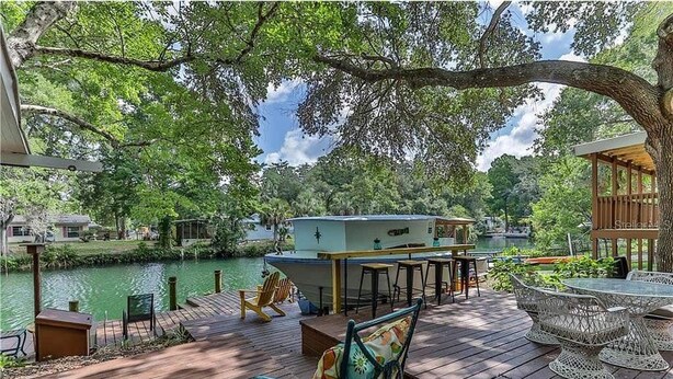 A wooden deck with outdoor seating, a boat house, and a view of a river. - Fun Weeki Wachee River Boathouse (Weeki Wachee)