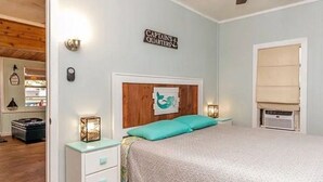 A bedroom with a bed, a nightstand, a dresser, a wall-mounted sign, and a window with a blind. - Fun Weeki Wachee River Boathouse (Weeki Wachee)