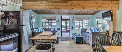 A kitchen with a wooden ceiling, a refrigerator, a stove, and a dining area with a table and chairs.