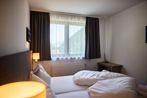 Habitación de hotel con cama, mesita de noche, lámpara y ventana con cortinas.