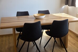 Una mesa rectangular de comedor con tapa de madera y cuatro sillas negras con patas de metal. Sobre la mesa, un cuenco blanco.