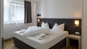 A neatly made bed with white linens, a bedside table with a lamp, and a window with sheer curtains. - 4805 Cirrus 5 (St. Gallenkirch)