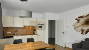 Une cuisine moderne avec des meubles blancs, une table à manger en bois et un canapé gris.
