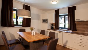 Een moderne keuken met een eethoek, houten kastjes, een magnetron en een groot raam met gordijnen.