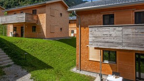 Une maison moderne en bois avec un balcon, une petite table et une chaise à l’extérieur.