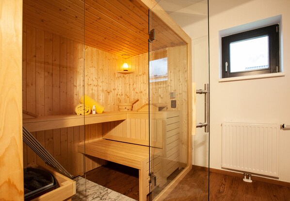 A sauna room with wooden walls, a glass door, a bench, and a small window.