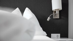 A modern hotel room with a grey textured headboard, a bedside table with a lamp, and a power outlet. - 46142 Montan 14 OG (St. Gallenkirch)