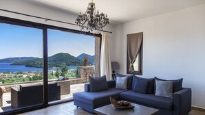 A modern living room with a large window offering a scenic view of a lake and mountains. - Villa Kallisto with Infinity Pool & Stunning Sea View in Perigiali, Lefkada!!! (Perigiali)