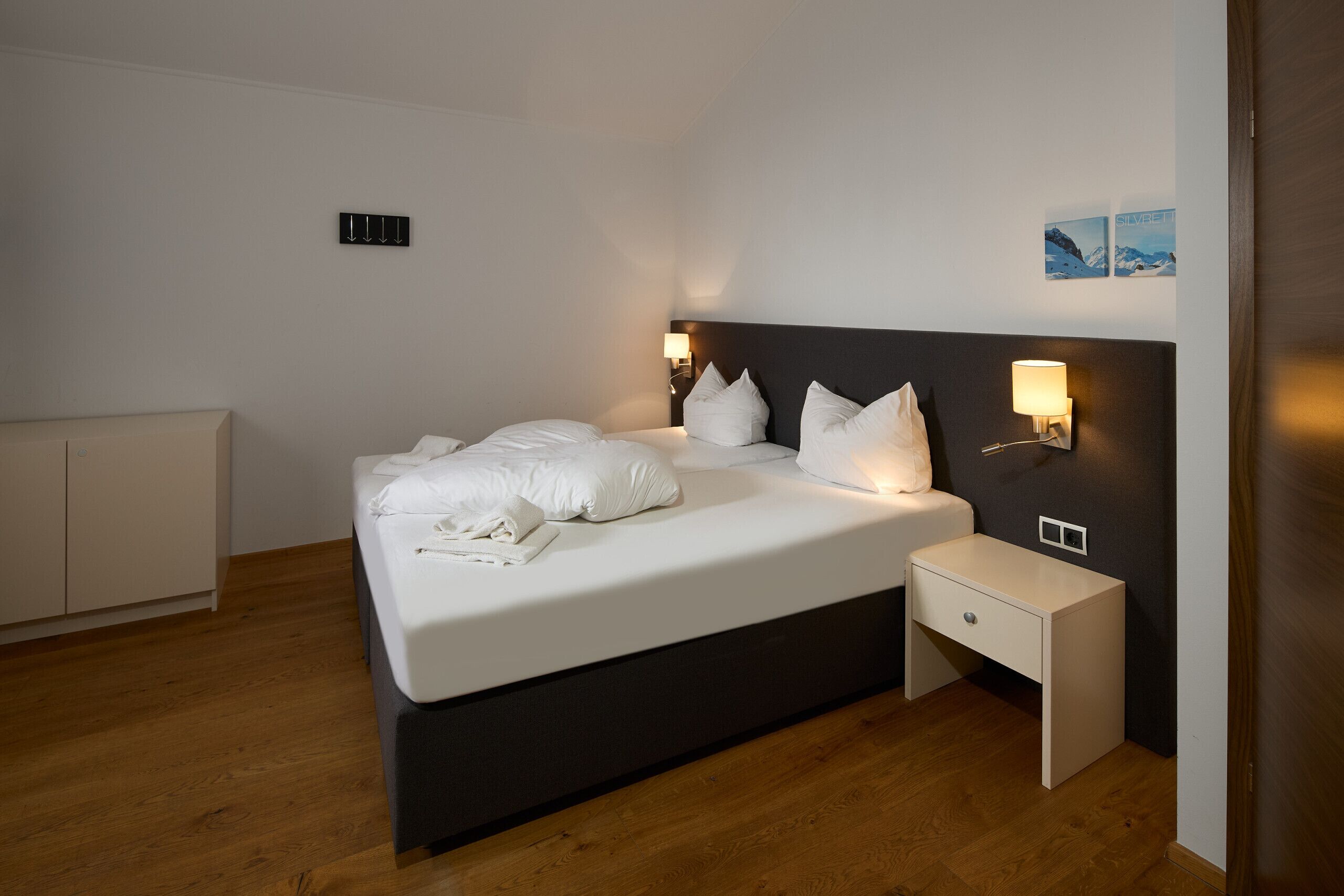Una habitación de hotel moderna con una cama grande, mesitas de noche, un armario y una lámpara fijada a la pared.