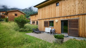 A wooden house with a patio, two lounge chairs, and a small table.