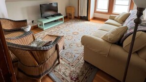 Ein gemütliches Wohnzimmer mit einer Couch, einem Fernseher, einem Holzstuhl und einem gemusterten Teppich.