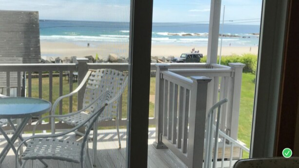 Ein Balkon mit Tisch und Stühlen, der Blick auf einen Strand mit Wellen und einem klaren Himmel bietet.