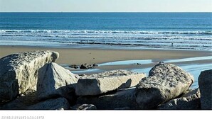 Ein Strand mit großen Felsen im Vordergrund und freiem Blick auf den Ozean.