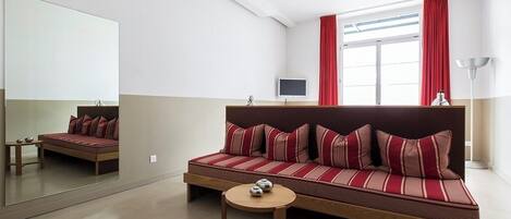 A modern room with a sofa, a small table, a TV, and a large mirror.
