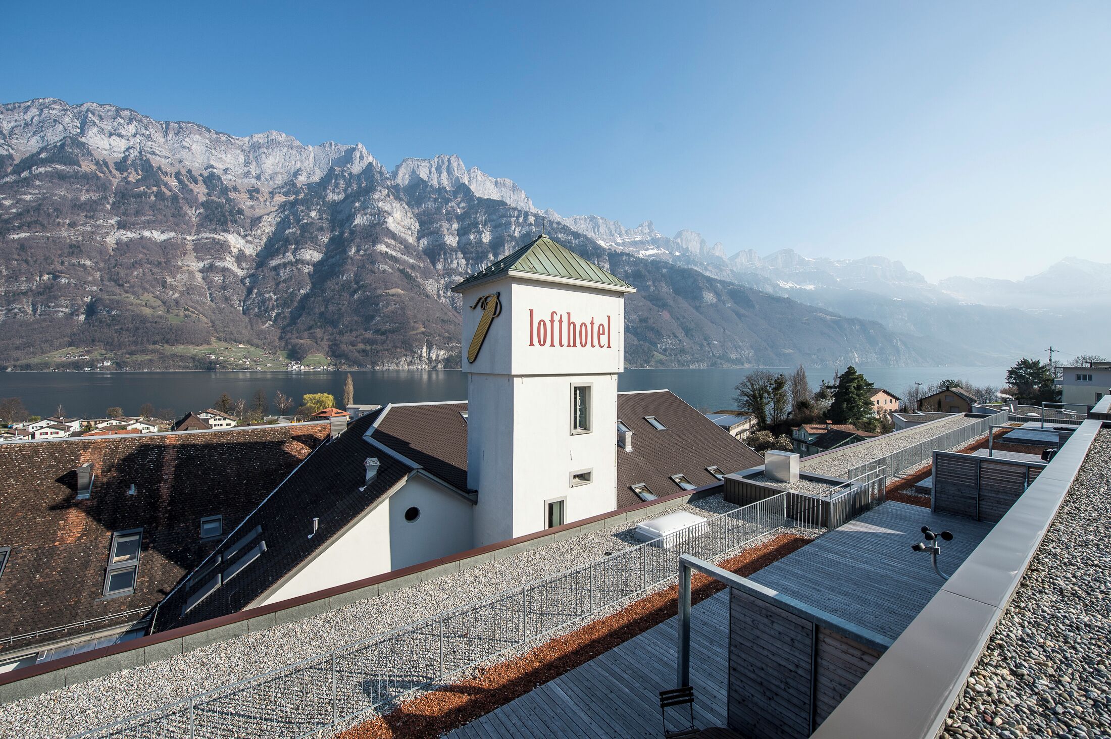 A hotel with a rooftop terrace, a sign reading 'lofhotel,' and a mountainous backdrop.