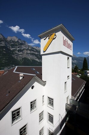 A hotel named 'Lofthotel' with a distinctive yellow and red sign, set against a backdrop of mountains and clear skies.