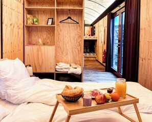 A wooden room with a bed, a tray with food and drink, and a view of the outside.