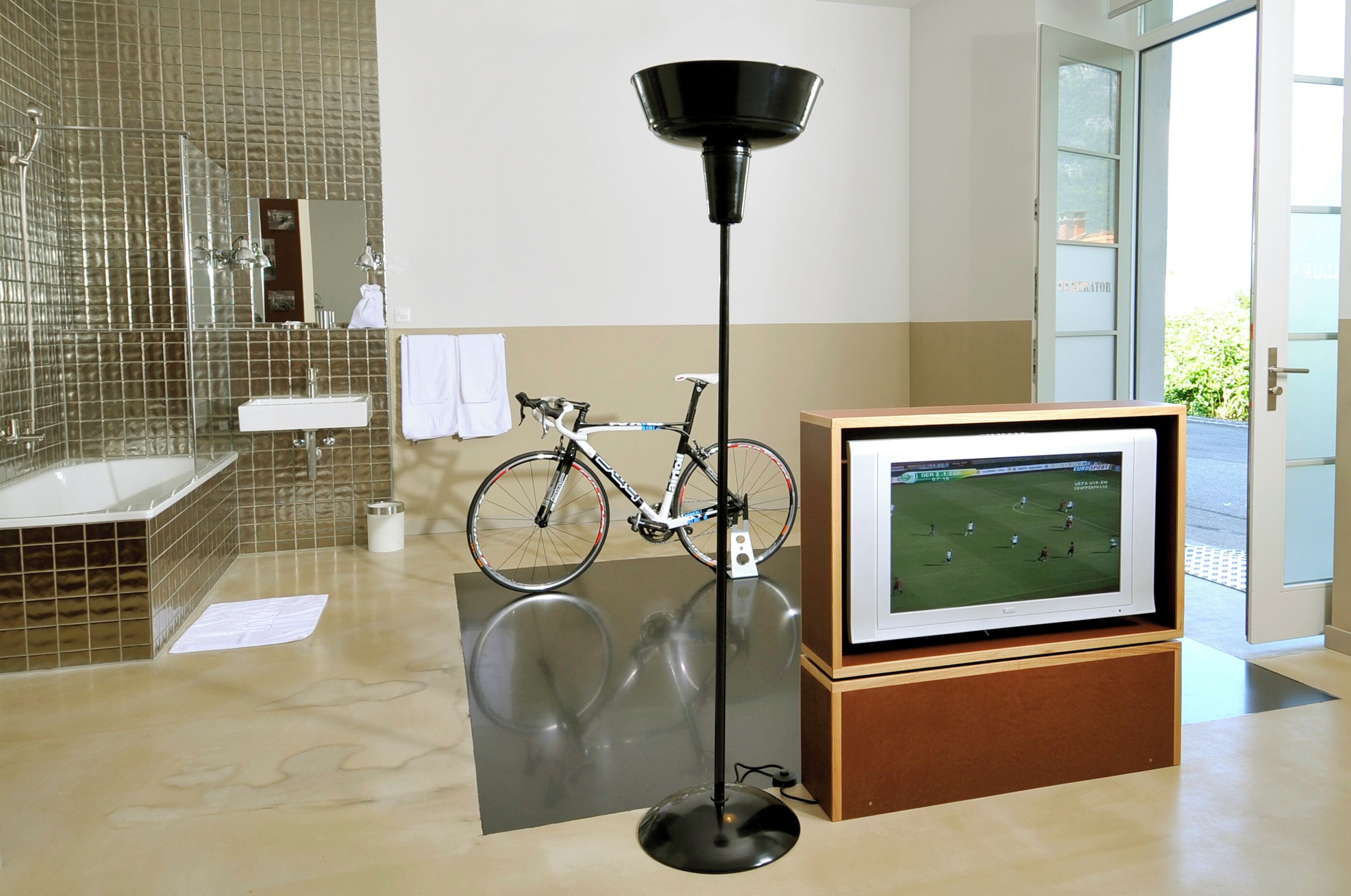 Un bany amb banyera, mirall, bicicleta i pantalla de televisió.