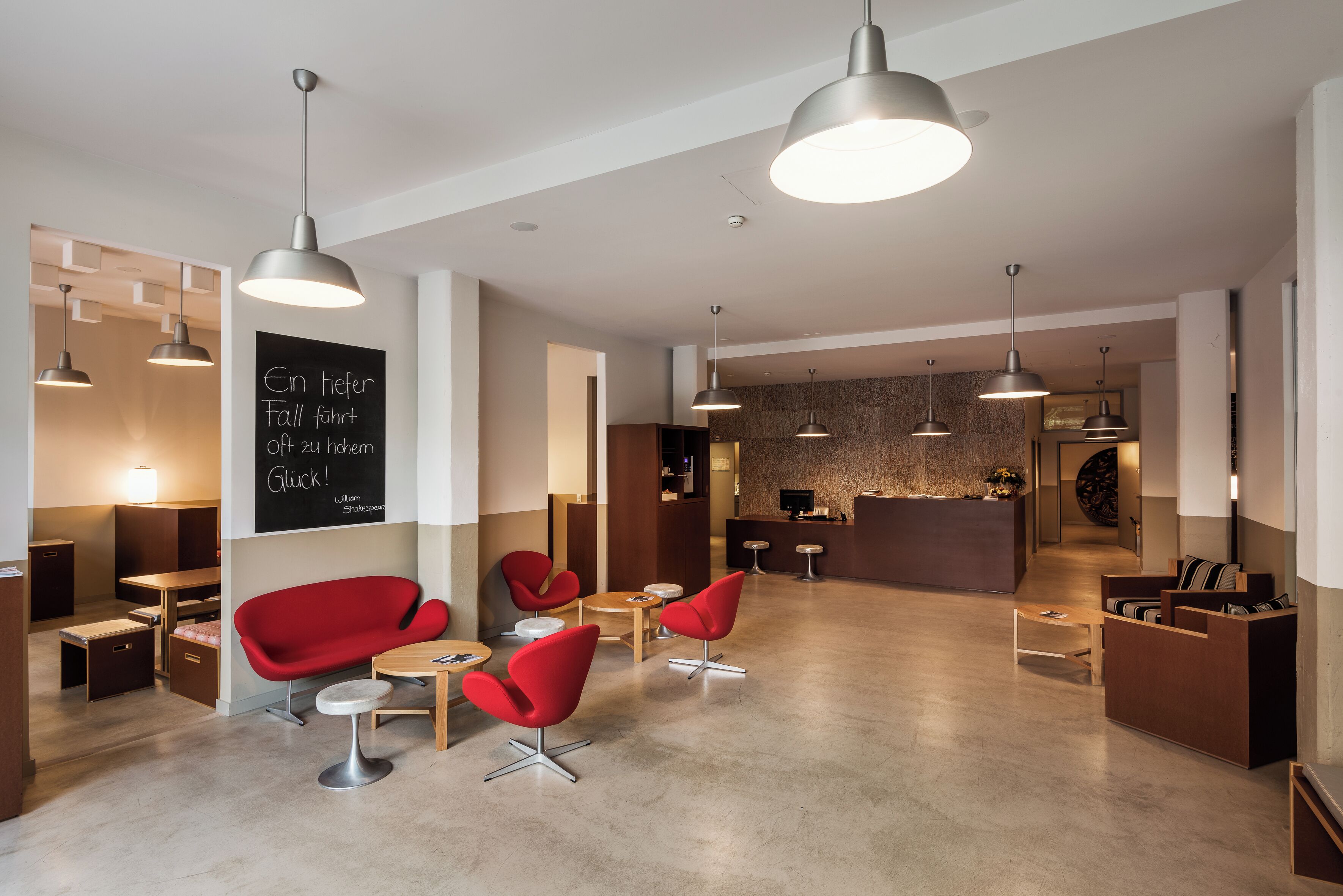 A modern interior with red chairs, a reception desk, and pendant lighting.