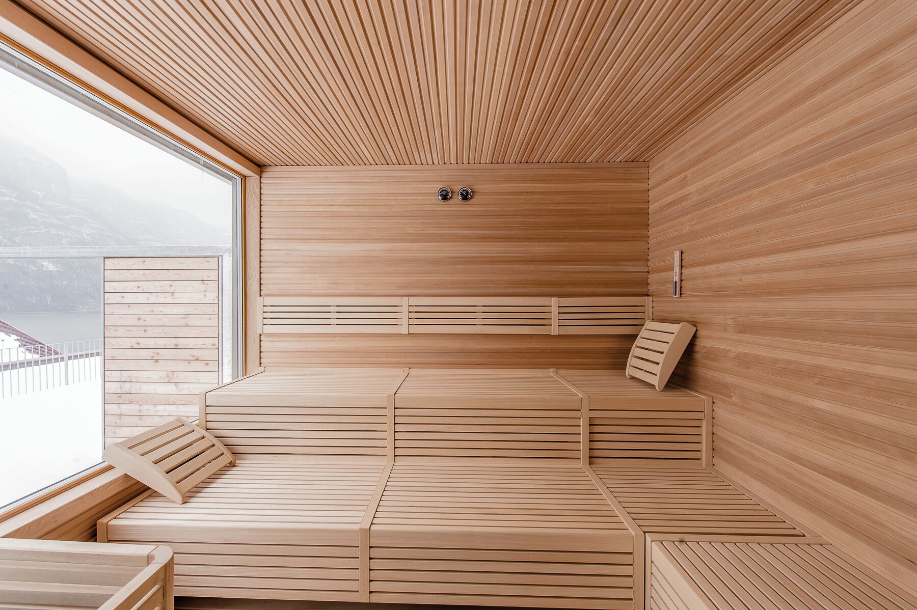 Eine Sauna mit Holzbänken und schrägverdeckter Decke, ein Fenster mit Bergblick und eine kleine Ablagefläche mit Gegenständen.