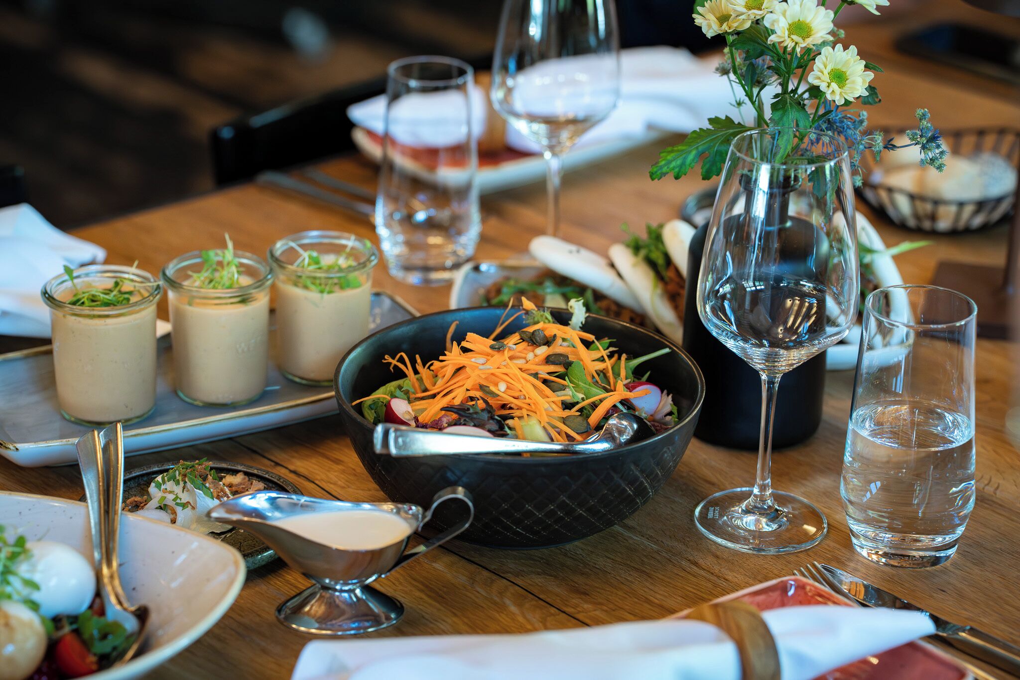 A dining table with a salad, drinks, and a vase of flowers.