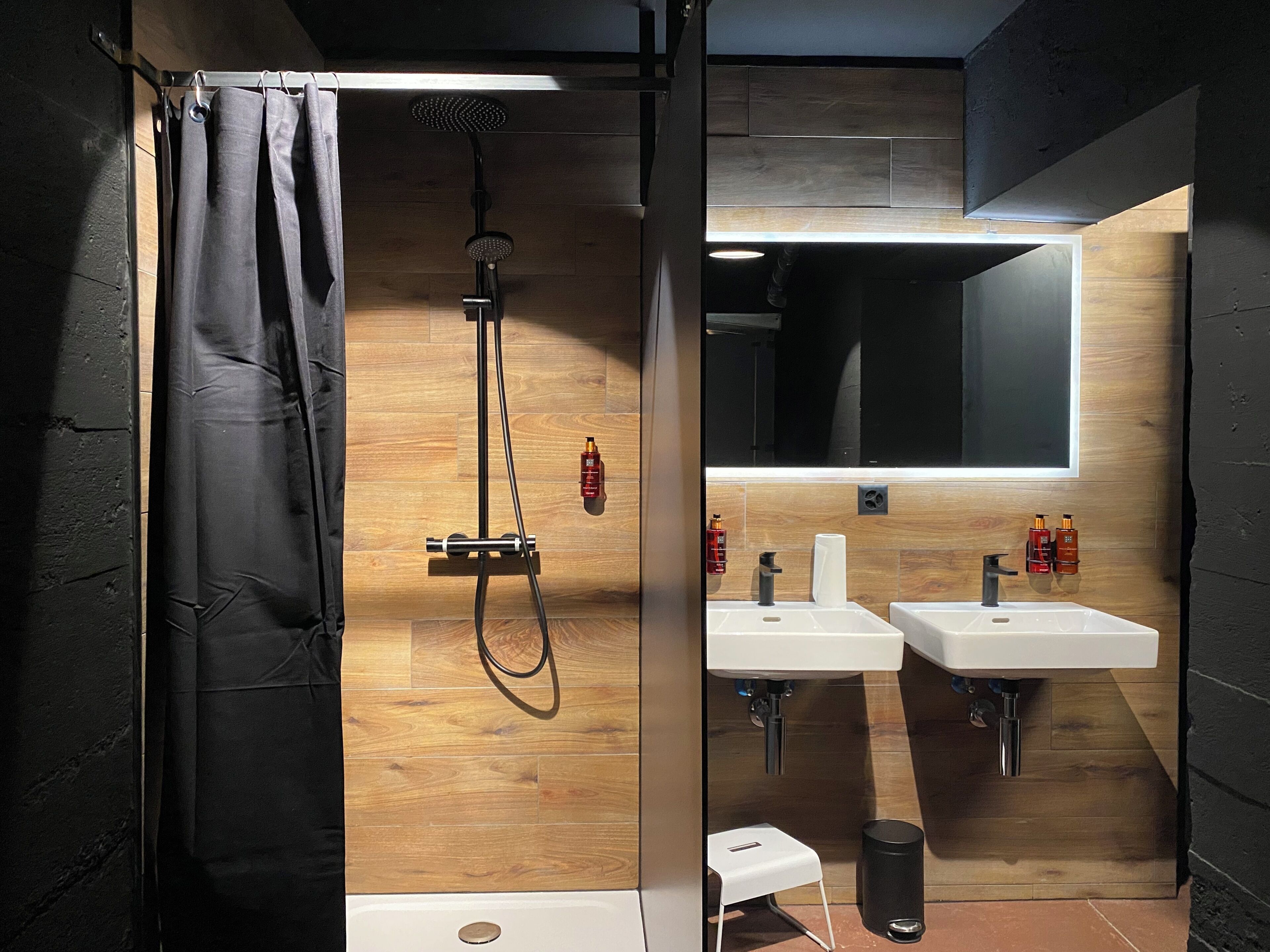 Un baño moderno con ducha, dos lavamanos, un espejo y un taburete pequeño.