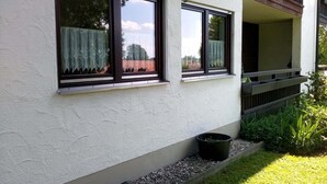 A building with two windows, a small garden area with a planter, and a balcony. - Ferienwohnung, 35 qm Erdgeschoss, Kombinierter Wohn- und Schlafraum (Bad Endorf)