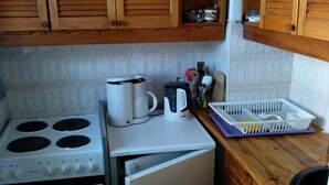 A kitchen with wooden cabinets, a stove, a coffee maker, and a dish rack. - Ferienwohnung, 35 qm Erdgeschoss, Kombinierter Wohn- und Schlafraum (Bad Endorf)