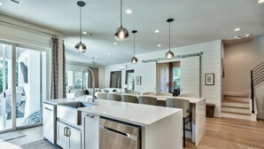 Una cocina moderna con una isla central, electrodomésticos de acero inoxidable, iluminación colgante y vistas al exterior.