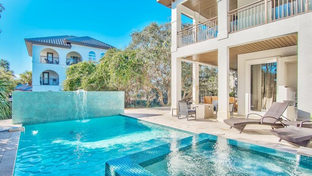 Una casa moderna de dos pisos con piscina, mobiliario exterior y vista a un edificio cercano.