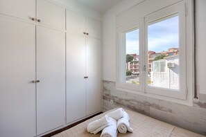 Une chambre avec des armoires blanches, une fenêtre donnant sur des immeubles et un lit avec des serviettes pliées.