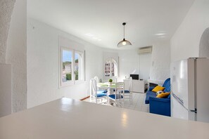 Eine moderne Küche mit weißen Schränken, ein Essbereich mit blauen Stühlen und ein blaues Sofa mit gelben Kissen.
