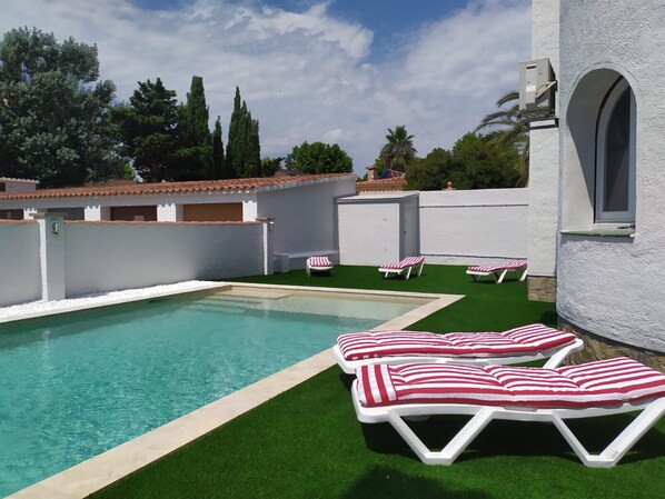 Une piscine bordée de gazon synthétique et agrémentée de chaises longues blanches avec des coussins à rayures rouges et blanches.
