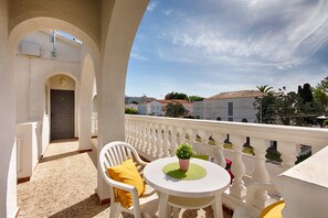 Un balcon avec une chaise blanche, une petite table sur laquelle est posée une plante en pot et un coussin jaune.