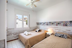 Une chambre avec deux lits, un ventilateur de plafond, une fenêtre et un mur recouvert de carreaux.