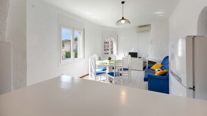 Una cocina moderna con muebles blancos, una zona de comedor con sillas azules y un sofá azul con cojines amarillos.