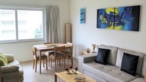 A living room with a sofa, a dining table with chairs, a coffee table, and artwork on the wall. - Ocean Breeze (Portimão)