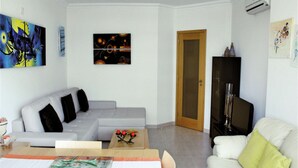 A modern living room with a grey sofa, a white sofa, a dining table with a placemat, and a TV stand. - Ocean Breeze (Portimão)