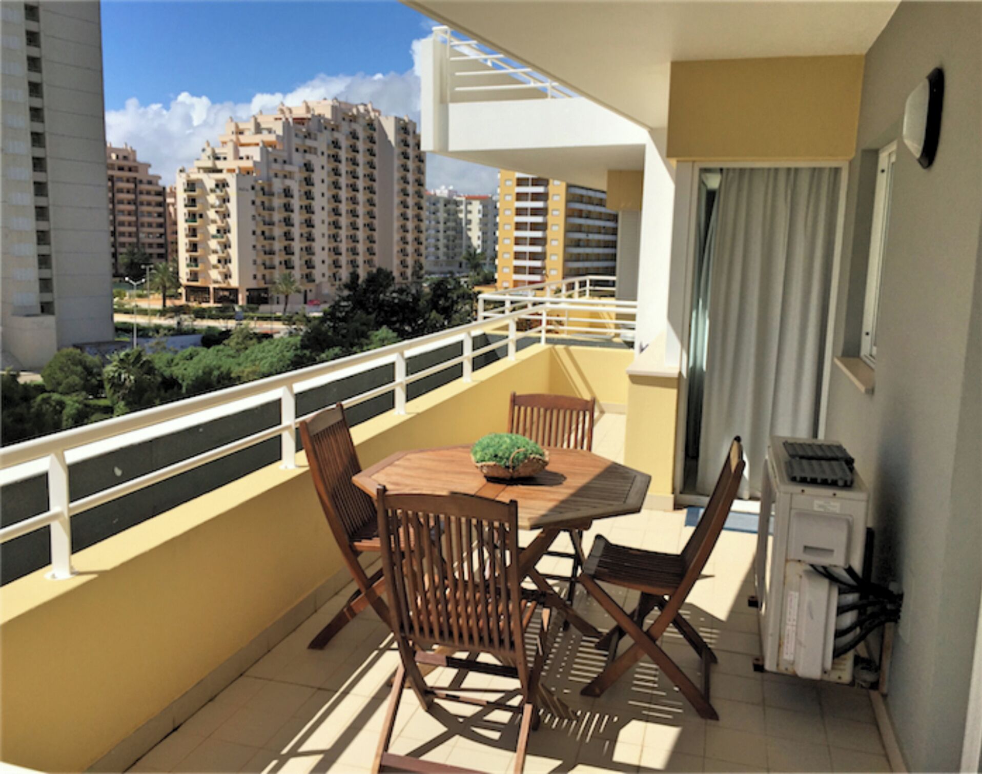 A balcony with a table and chairs, a potted plant, and a view of surrounding buildings.