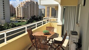 A balcony with a table and chairs, a potted plant, and a view of surrounding buildings. - Ocean Breeze (Portimão)