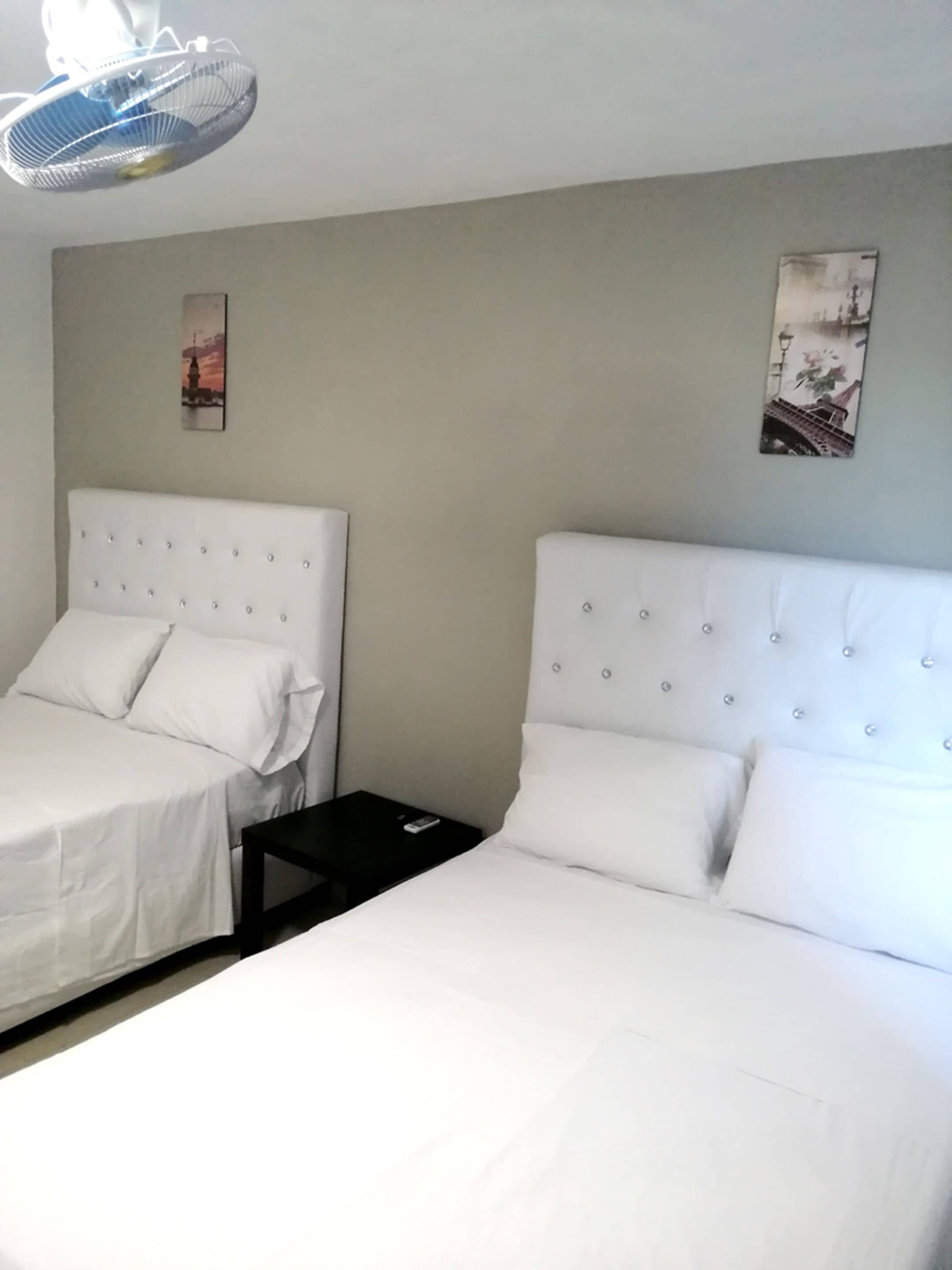 Habitación de hotel con dos camas, una mesita y un ventilador de techo.