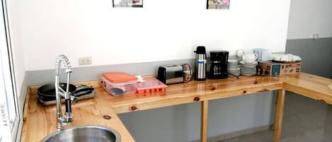 Una cocina con encimera de madera, pileta de acero inoxidable y diversos electrodomésticos, incluyendo una tostadora y una cafetera.