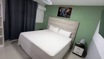 A neatly made bed with white linens in a room with green walls, a white ceiling fan, and a framed picture of an elephant.