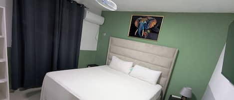 A neatly made bed with white linens in a room with green walls, a white ceiling fan, and a framed picture of an elephant.