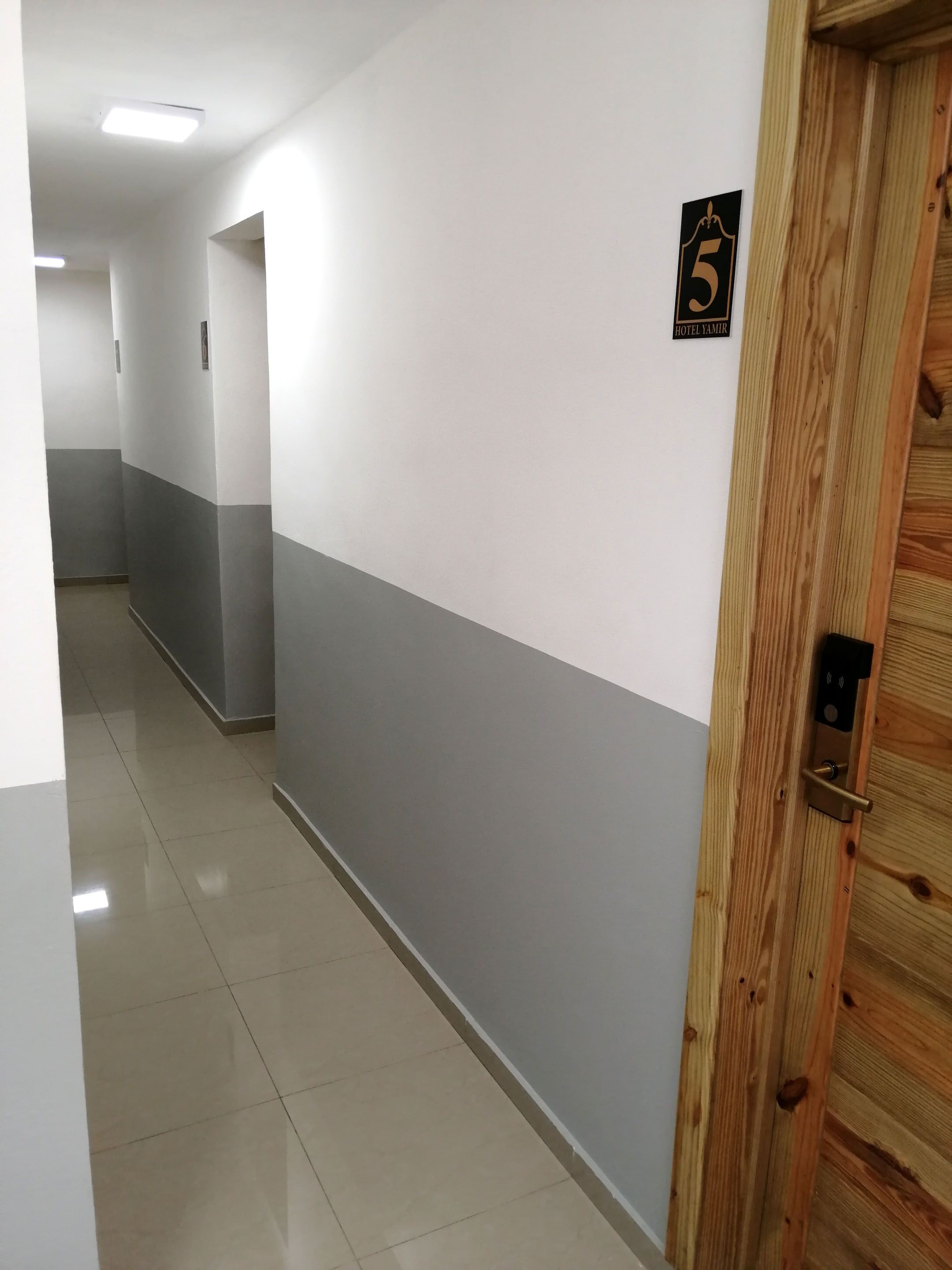 A hallway with a wooden door marked with the number 5, indicating a room or suite. The walls are painted in a two-tone color scheme, and the floor is tiled.