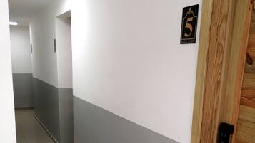 A hallway with a wooden door marked with the number 5, indicating a room or suite. The walls are painted in a two-tone color scheme, and the floor is tiled.