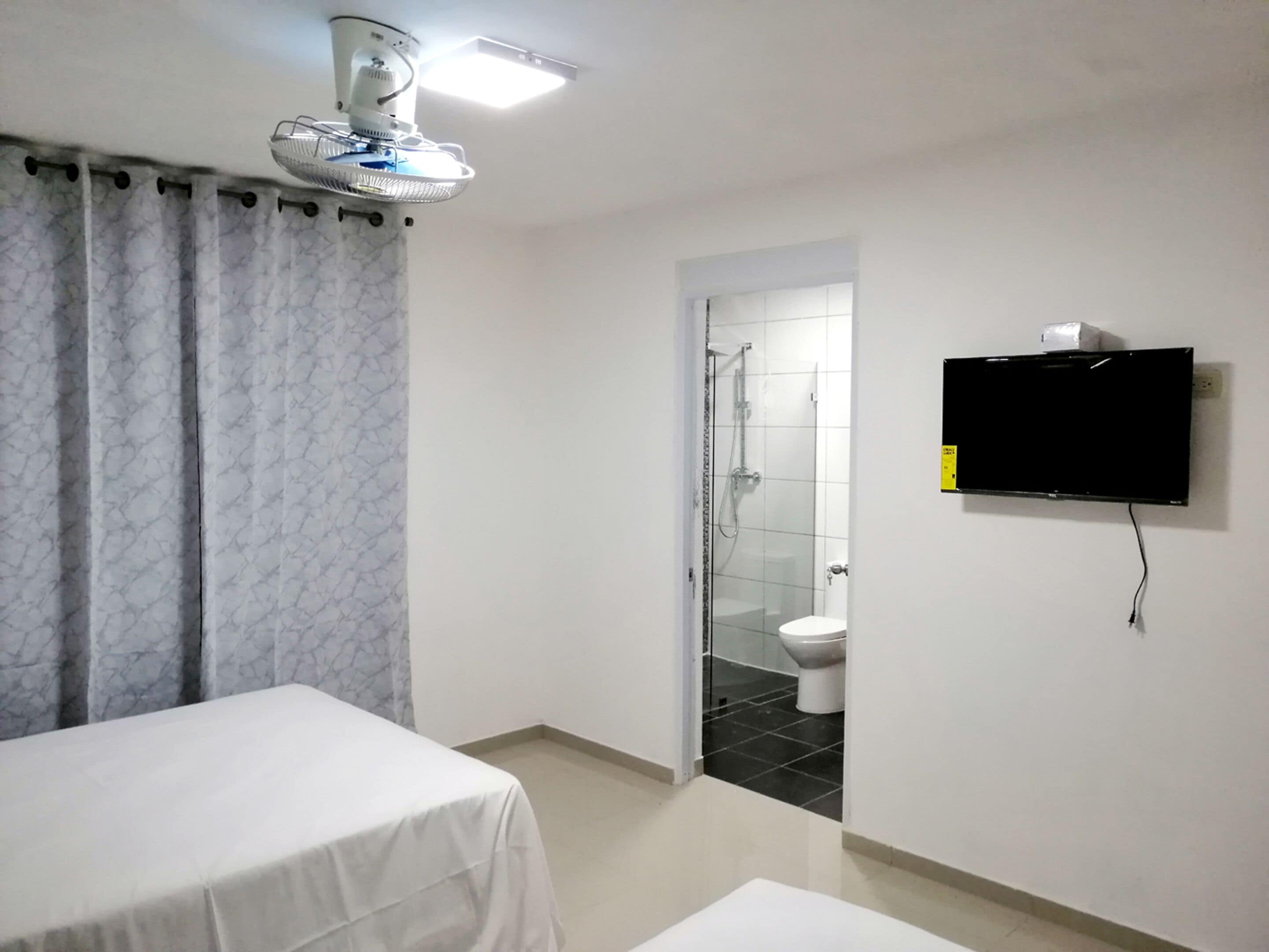 Una habitación de hotel con cama, televisor montado en la pared, zona de ducha y un inodoro.